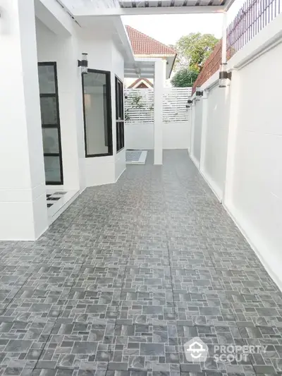 Pristine white-walled home with a stylish grey-tiled outdoor walkway, offering a sleek and modern entrance experience, nestled in a serene residential area.