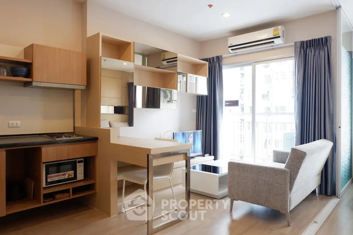 Modern living room with open kitchen, stylish furniture, and natural light from large windows.
