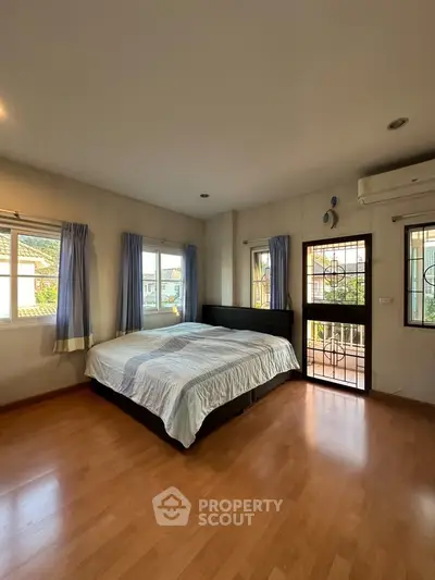 Spacious bedroom with large windows and balcony access, featuring wooden flooring and modern decor.