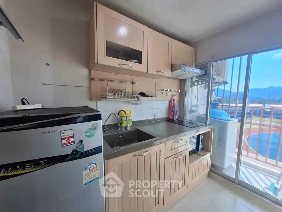 Modern kitchen with sleek cabinets and balcony view, featuring a compact fridge and stainless steel sink.