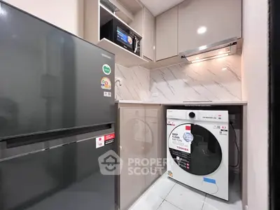 Modern kitchen with sleek appliances including fridge and washing machine in compact layout.