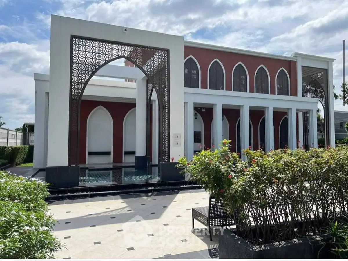 Elegant building exterior with intricate arch design and lush landscaping under a bright sky.