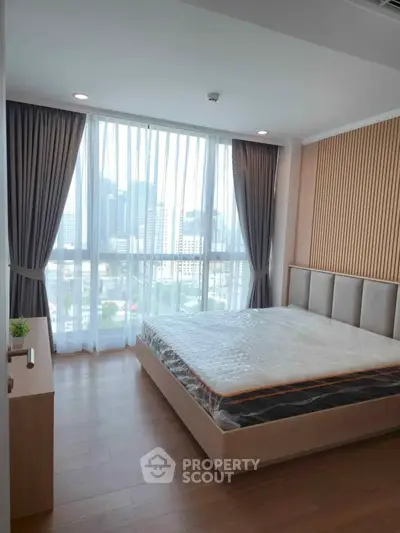 Modern bedroom with large window and city view, featuring elegant curtains and wooden flooring.