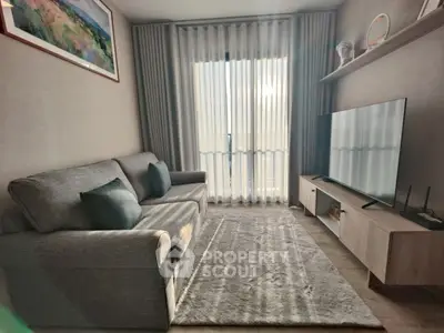 Cozy living room with modern decor, large TV, and natural light through sheer curtains.