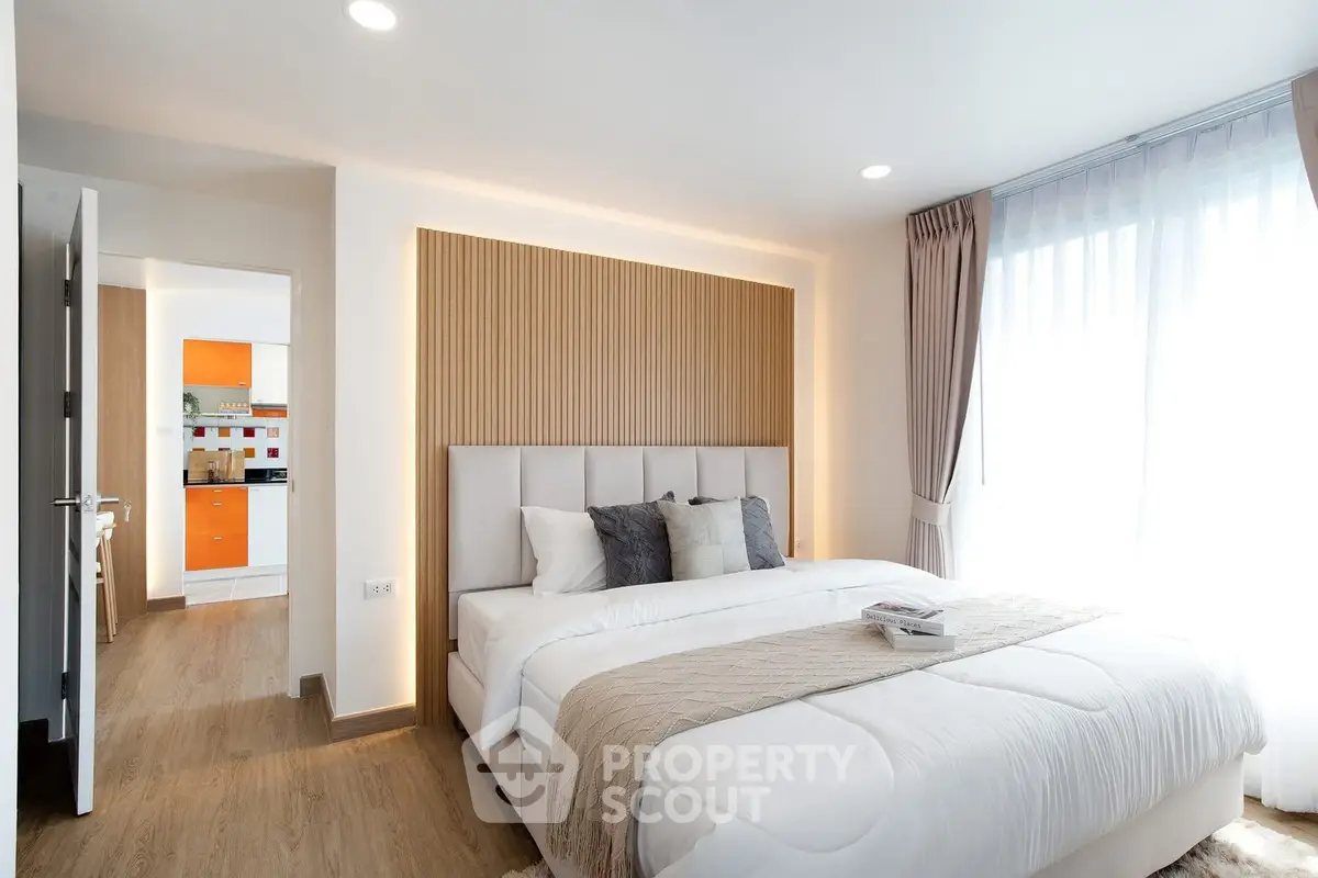Modern bedroom with cozy bed and stylish decor, adjacent to a bright kitchen area.