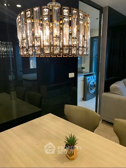 Modern dining area with elegant chandelier and view into a stylish living room with washing machine.
