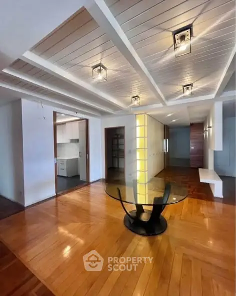 Spacious modern living room with wooden flooring and stylish ceiling lights, featuring a sleek glass dining table.