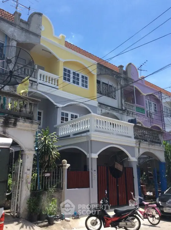 Colorful townhouse exterior with balconies and motorbike in front, vibrant urban living.