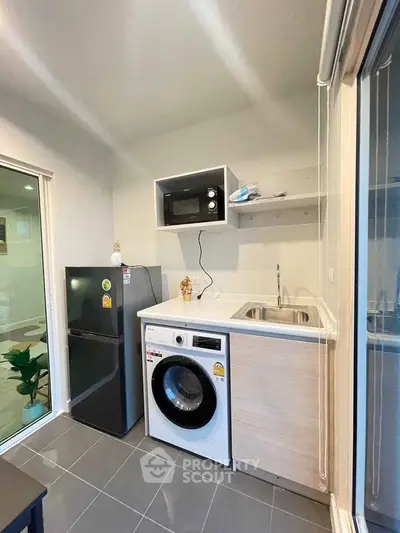 Modern compact kitchen with washing machine and microwave in sleek apartment.