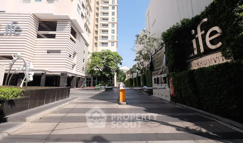 Modern condominium entrance with sleek design and lush greenery in urban setting.