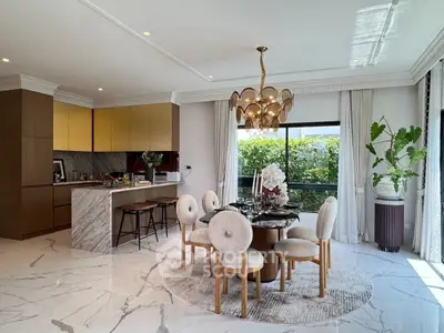 Luxurious dining area with elegant chandelier and open kitchen layout, featuring marble flooring and lush garden view.