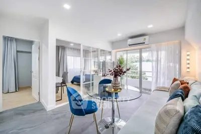 Modern living room with glass table, blue chairs, and cozy sofa leading to a bright bedroom.