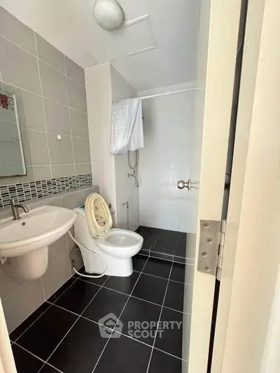 Modern bathroom with sleek black tiles and a compact layout, featuring a shower and stylish sink.