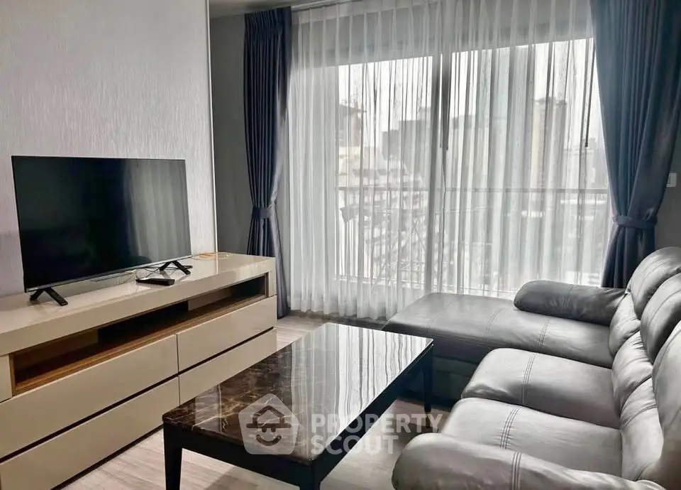Modern living room with sleek furniture and large window offering city views.
