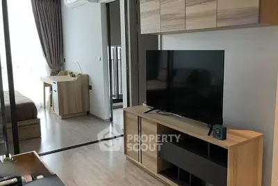 Modern living room with sleek wooden furniture and large TV, adjacent to a cozy bedroom.