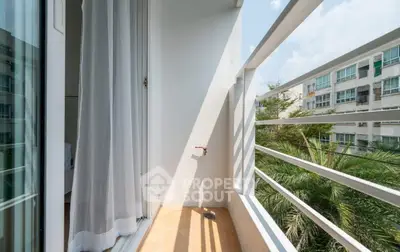 Charming small balcony with serene view of lush greenery and modern building exterior.