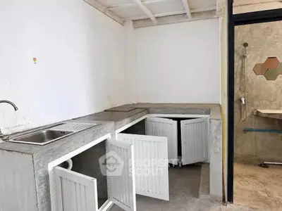 Minimalist kitchen with concrete countertops and open cabinets, adjacent to a modern shower area.