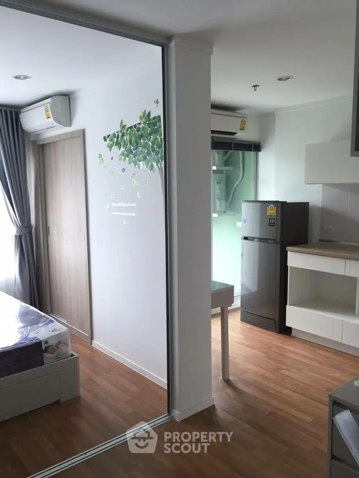 Modern studio apartment with wooden flooring, compact kitchen, and natural light.