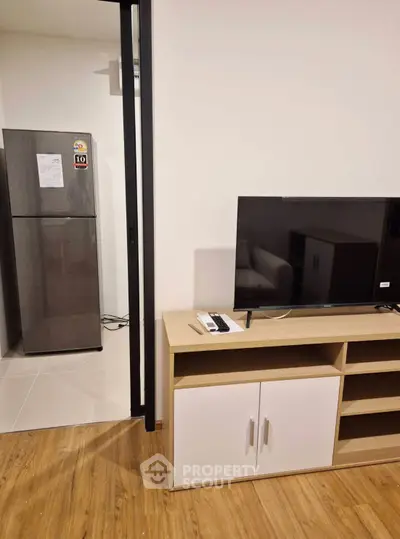 Modern apartment interior with sleek TV stand and stainless steel fridge, showcasing contemporary living space.