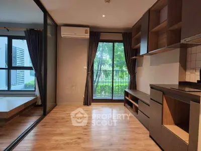 Modern apartment interior with open layout, wooden flooring, and large windows overlooking greenery.