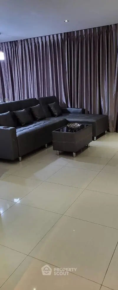 Spacious modern living room with sleek leather sofa and elegant floor-to-ceiling curtains.