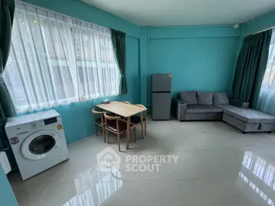 Spacious living room with modern sofa, dining set, washing machine, and fridge in bright teal decor.