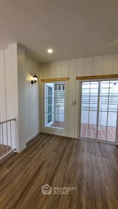 Charming interior with wooden flooring and large windows leading to a balcony, perfect for natural light lovers.