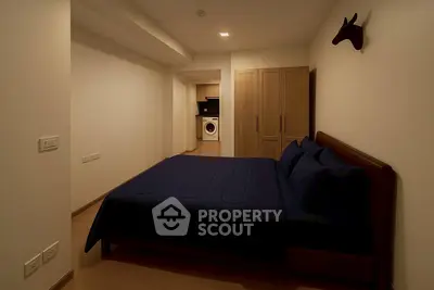 Modern bedroom with dark bedding and in-room washing machine, featuring sleek wooden wardrobe and minimalist decor.