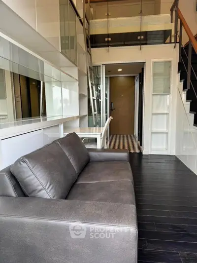 Modern loft-style living room with sleek leather sofa and elegant staircase