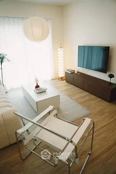 Modern living room with stylish furniture and large TV, featuring wooden flooring and natural light.