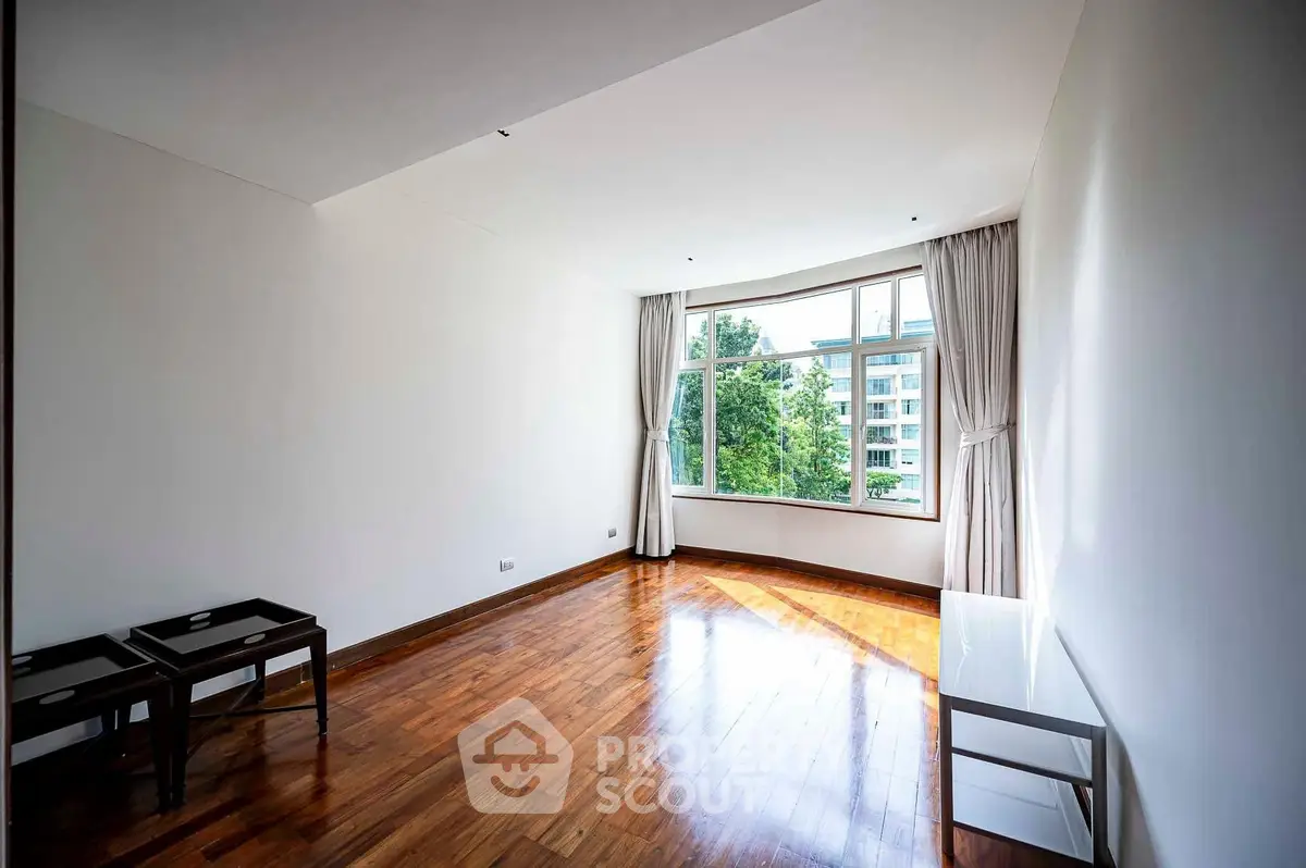 Spacious empty room with large window and hardwood floors, perfect for customization.