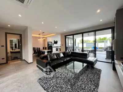 Luxurious open-plan living room with modern black leather sofa and glass coffee table, leading to a spacious outdoor patio.