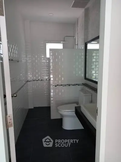 Modern bathroom with sleek design and white tiles, featuring a shower and toilet.