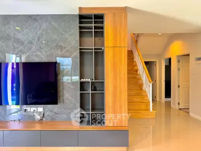 Modern living room with sleek wooden shelving and staircase, featuring a mounted TV and glossy flooring.