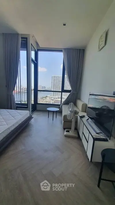 Modern bedroom with large windows offering stunning city views, featuring a cozy bed and sleek TV setup.