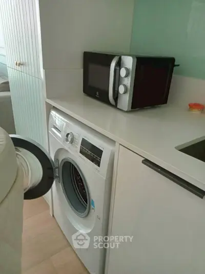 Modern kitchen with washing machine and microwave, sleek cabinetry, and stylish countertop.