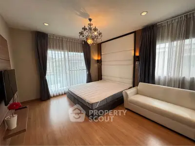 Elegant bedroom with chandelier, large windows, and cozy seating area.