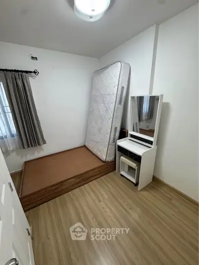 Minimalist bedroom with wooden flooring and a mattress against the wall, featuring a vanity table.