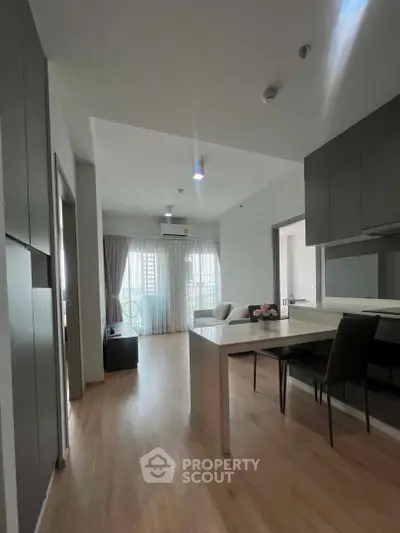 Modern open-plan living room with sleek kitchen and dining area, featuring natural light and contemporary design.