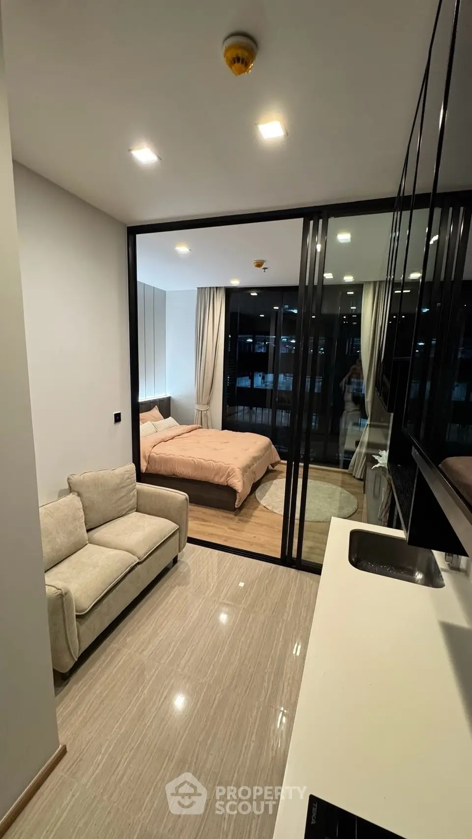 Modern studio apartment with open layout, featuring cozy living area and elegant bedroom separated by glass partition.
