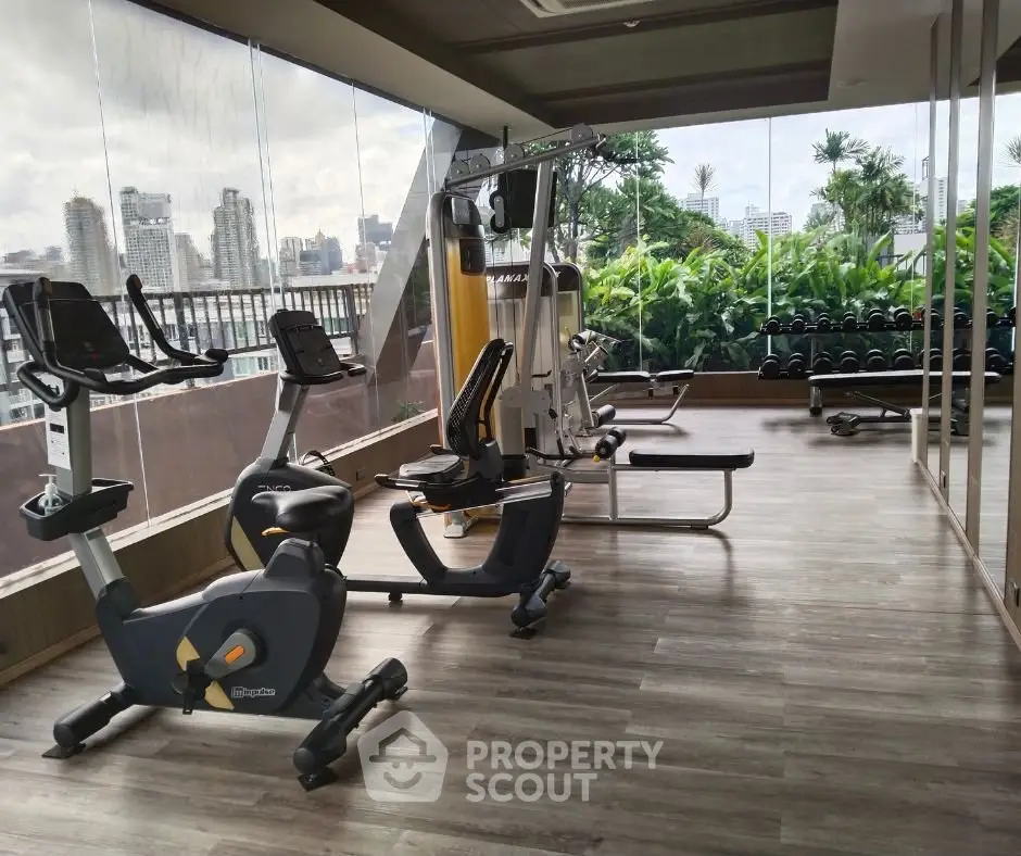Modern gym with city view, featuring state-of-the-art exercise equipment and lush greenery.