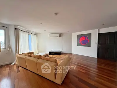 Spacious living room with hardwood floors and modern art, featuring a cozy beige sofa and large windows.