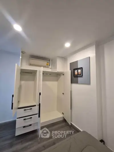 Modern bedroom with open wardrobe and air conditioning unit, showcasing sleek design and ample storage space.