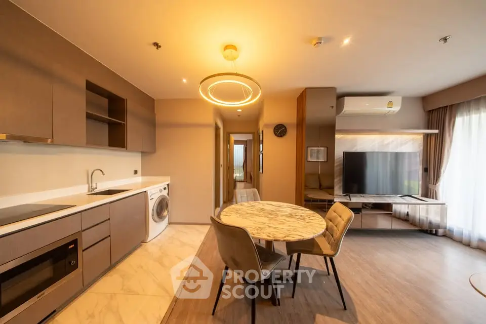 Modern living room with stylish furniture and open kitchen layout, featuring a washing machine and elegant lighting.