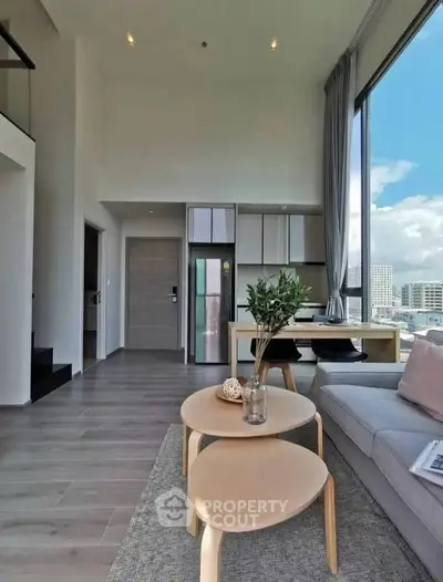 Modern living room with high ceilings and city view, featuring stylish furniture and large windows.
