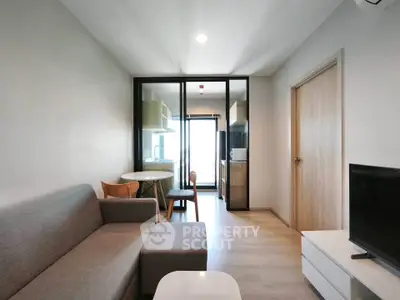 Modern living room with sleek furniture and glass partition leading to kitchen area.