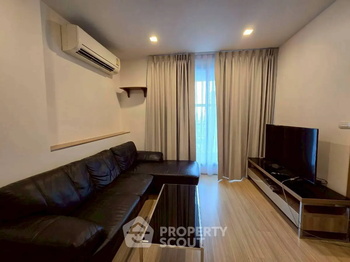 Modern living room with sleek black leather sofa and large TV, featuring elegant wooden flooring and ambient lighting.