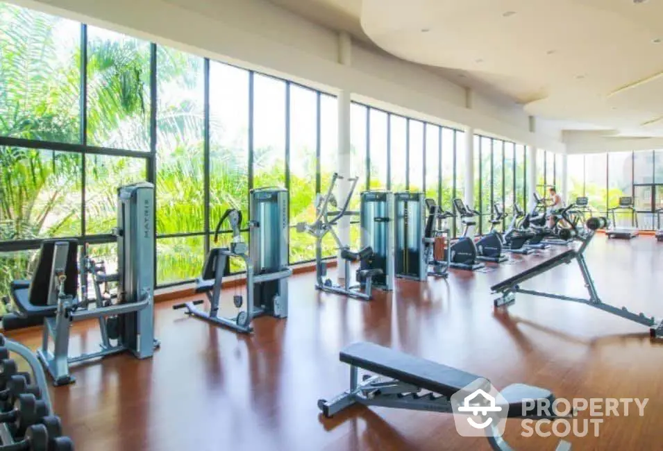 Spacious gym with modern equipment and large windows offering lush green views.