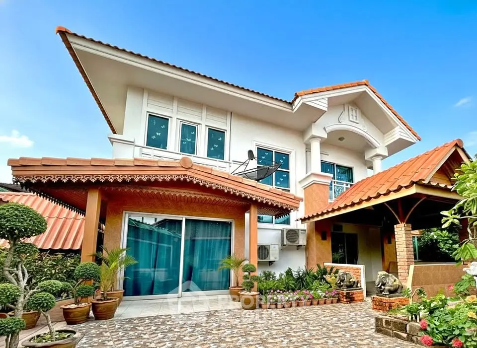 Charming two-story house with terracotta roof, lush garden, and spacious driveway under a clear blue sky.