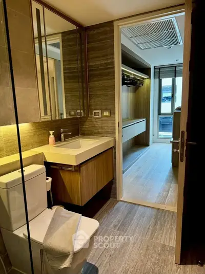 Modern bathroom with sleek design leading to a walk-in closet, featuring elegant wood finishes and ample natural light.